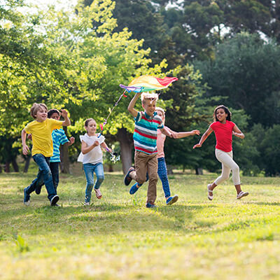Several children in a park running while playing with a colorful kite